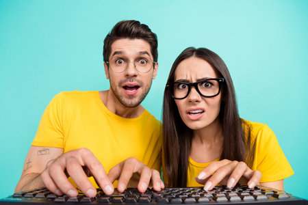 Closeup portrait of young geeks it specialists wear yellow t-shirt writing keyboard browsing esport betting isolated on aquamarine color backgroundの写真素材