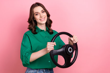 Portrait of positive pleasant lovely girl with curly hairstyle wear green shirt holds steering wheel isolated on pink backgroundの写真素材
