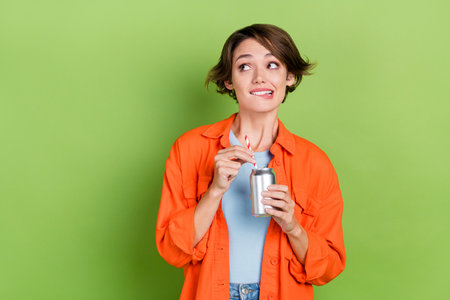 Photo of funny doubtful woman wear denim jacket drinking coke looking empty space isolated green color backgroundの写真素材