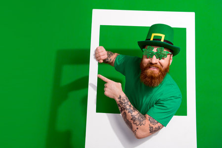 Photo of funky positive man wear t-shirt enjoying shamrock day tacking photography empty space isolated green color backgroundの写真素材