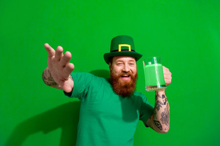 Photo of handsome carefree guy dressed t-shirt cap celebrating clover day drinking ale beer isolated green color backgroundの写真素材
