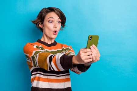 Portrait of impressed speechless girl with bob hair wear striped pullover look at phone open mouth isolated on blue color backgroundの写真素材
