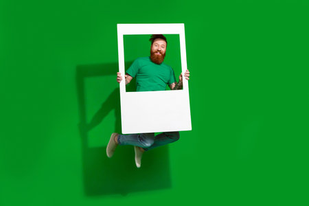 Full body portrait of active cheerful person jumping hands hold paper album card isolated on green...