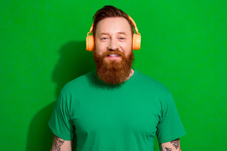 Photo of attractive cheerful man wear t-shirt smiling enjoying songs headphones isolated green color backgroundの写真素材