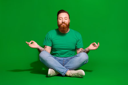 Full length photo of funky dreamy guy dressed t-shirt closed eyes practicing yoga isolated green color backgroundの写真素材