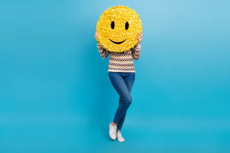 Full body portrait of lady arms hold large smiley emoji collage cover hide face isolated on blue color backgroundの写真素材