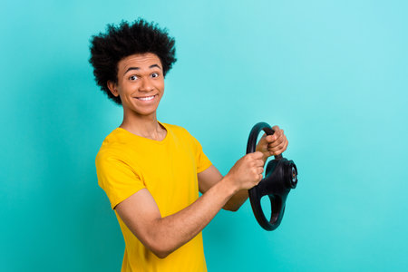 Portrait of optimistic satisfied guy wear yellow t-shirt holding steering wheel buy new car isolated on vibrant teal color backgroundの写真素材