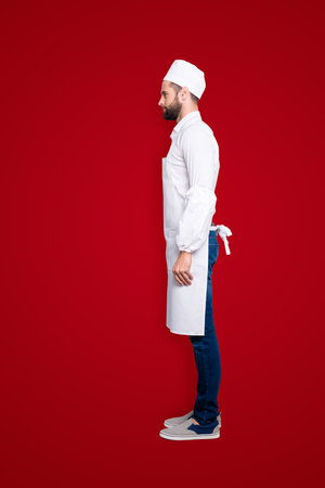 Profile side view snap, full size body portrait of attractive handsome butcher isolated over grey background, wearing white shirt, apron, jeans, sneakersの写真素材