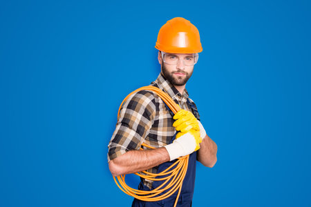 Portrait of trendy virile electrician in hardhat, overall, shirt is ready for work, having, holding...