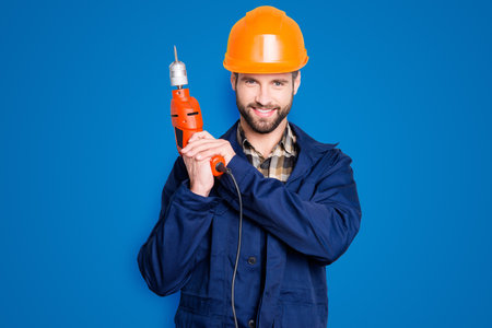 Portrait of joyful positive repairer in protective hard hat with stubble showing, having equipment...