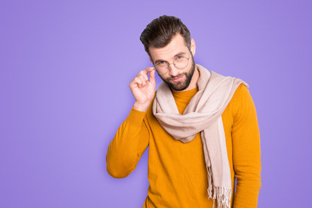Portrait of modern confident stylist with scarf around neck looking out glasses at camera isolated on grey background holding hand on eyelet of spectacles on his faceの写真素材