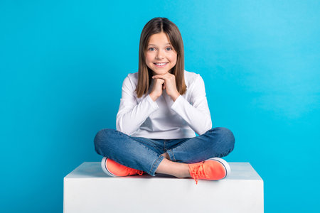 Photo of dreamy sweet small lady dressed white shirt sitting legs crossed smiling isolated blue color backgroundの写真素材