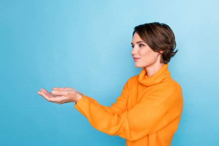 Profile portrait of lovely positive person arms palms hold empty space isolated on blue color backgroundの写真素材