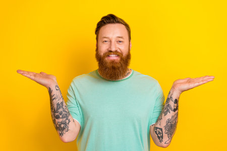 Photo of young stylish wearing man green t-shirt long red beard balance alternative product choose crisis time isolated on yellow color backgroundの写真素材