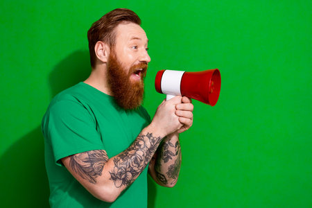 Photo of cool excited guy dressed t-shirt screaming bullhorn empty space isolated green color backgroundの写真素材