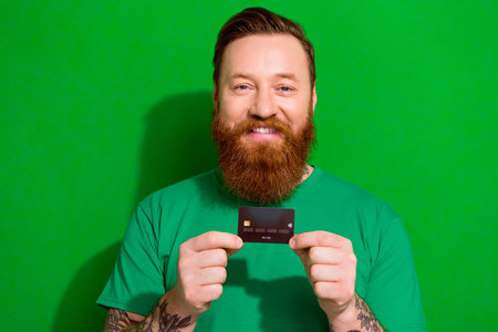 Portrait of brutal good mood man with red beard wear trendy t-shirt holding plastic credit card...