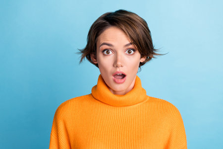 Photo portrait of attractive young woman astonished hear shocking news dressed stylish orange clothes isolated on blue color backgroundの写真素材