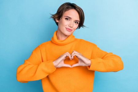 Photo portrait of pretty young girl showing fingers heart love gesture feedback wear trendy orange look isolated on blue color backgroundの写真素材