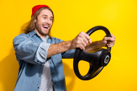 Photo of funny excited guy dressed jeans shirt driving car empty space isolated yellow color backgroundの写真素材
