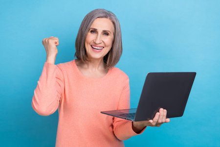 Photo of lucky excited lady dressed coral shirt rising fist typing modern device isolated blue color...