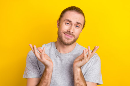 Photo of friendly confused handsome man with long hairstyle wear gray t-shirt hold palms has no idea isolated on yellow color backgroundの写真素材