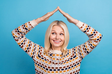 Photo of thoughtful positive lady dressed pullover showing arms roof looking empty space isolated blue color backgroundの写真素材