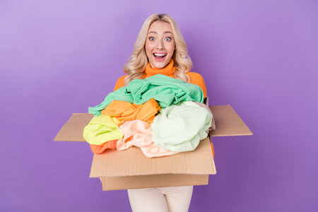 Photo of astonished funky girl hold carton box pile stack clothes isolated on violet color...