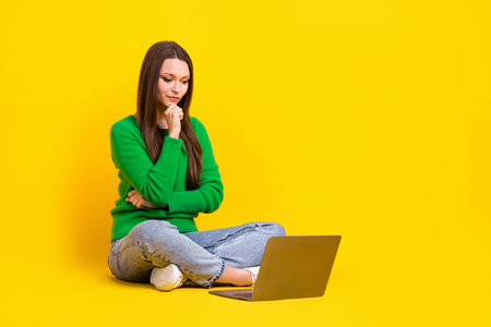 Full length photo of sweet thoughtful woman wear green sweater working modern device empty space isolated yellow color backgroundの写真素材