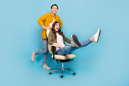 Full body length photo cadre of funny overjoyed playing couple push boss chair comfort activity fast speed moving isolated on blue color backgroundの写真素材