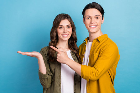 Photo of sweet positive married couple wear shirts pointing holding arm empty space isolated blue color backgroundの写真素材