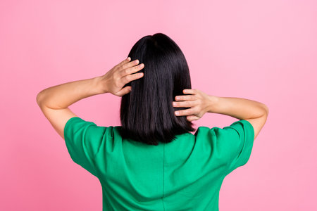 Back view photo of gorgeous adorable woman straight hairstyle oversize t-shirt arms touching soft hair isolated on pink color backgroundの写真素材