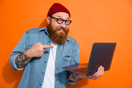 Photo of funky young guy holding netbook pointing finger demonstrate website discounts sale isolated on shine color backgroundの写真素材