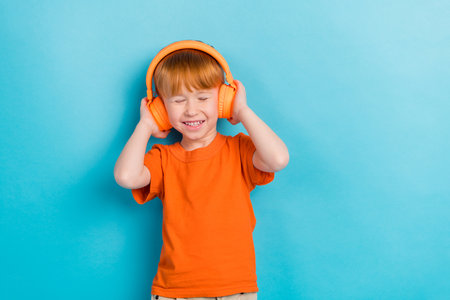 Photo of funky crazy positive boy wear stylish orange clothes enjoy track song quality sound empty space isolated on cyan color backgroundの写真素材