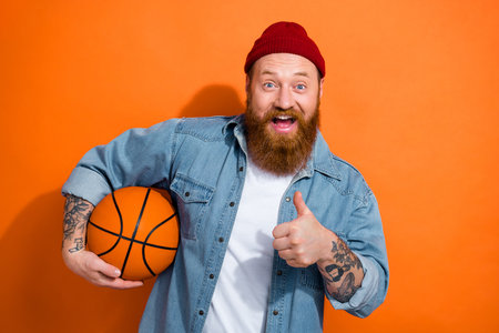Photo of funny surprised guy thumb up recommendation feedback rate hobby hold basketball sport fan betting advert isolated on orange color backgroundの写真素材