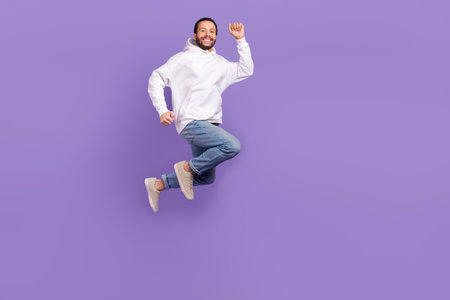 Full body picture of young overjoyed man running jumping feel his high speed promo new hoodie advert isolated on purple color backgroundの写真素材