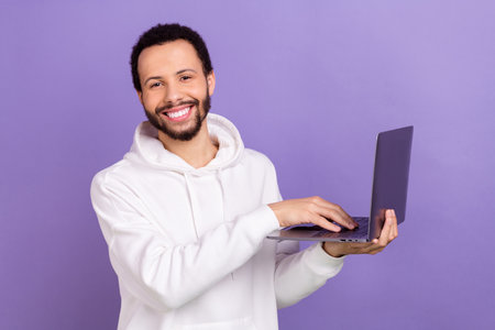Photo of handsome positive man toothy smile hold use netbook isolated on violet color backgroundの写真素材