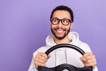 Portrait of young happy smile man wear sweatshirt driving steering wheel look empty space new rules isolated on purple color backgroundの写真素材