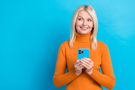 Portrait of gorgeous stunning glad woman wear orange stylish clothes hold modern device empty space isolated on blue color backgroundの写真素材