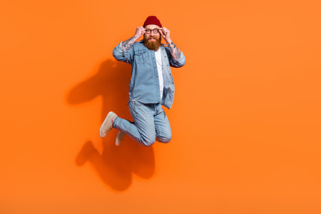 Full length portrait of cheerful carefree person jumping hands touch eyeglasses empty space isolated on orange color backgroundの写真素材