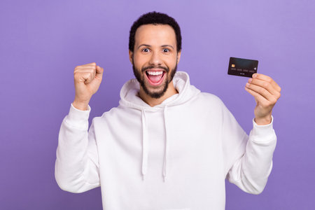 Portrait of ecstatic overjoyed guy with brunet beard wear white pullover hold credit card win...