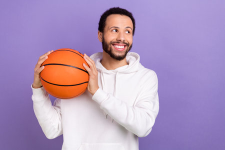 Portrait of positive minded man toothy smile hands hold basketball look empty space isolated on purple color backgroundの写真素材