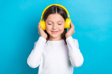 Photo of pretty shiny small lady dressed white shirt arms headphones closed eyes enjoying songs isolated blue color backgroundの写真素材
