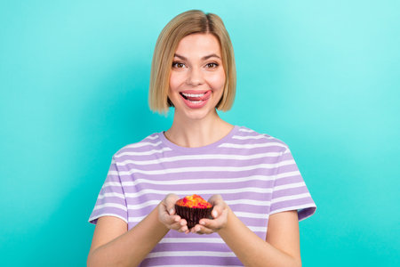 Photo of cheerful adorable girl short hairstyle striped t-shirt hold cake tongue licking teeth isolated on turquoise color backgroundの写真素材