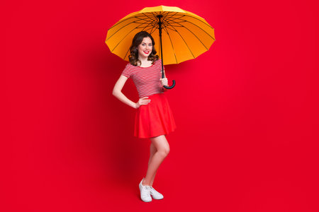 Full length photo of stunning cheerful lady wear stylish outfit hold parasol walking street enjoy summer time isolated red color backgroundの写真素材