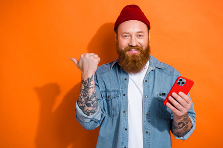 Photo of good mood guy dressed denim jacket texting empty space isolated orange color backgroundの写真素材