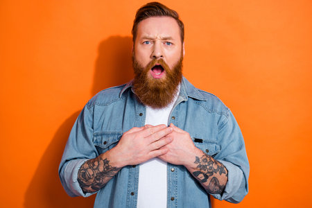 Photo of shocked young man hands touch chest open mouth stare disbelief isolated on orange color backgroundの写真素材