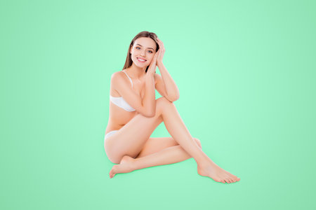 Portrait of thin slender woman sitting over white background in bra and bikini looking at camera demonstrating perfect body plain skinの写真素材