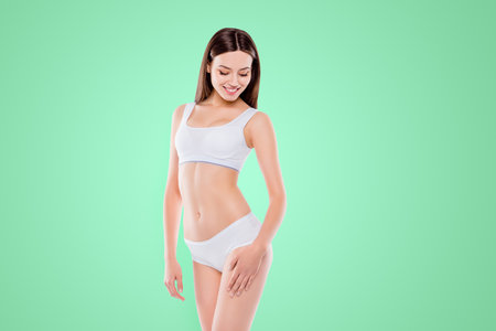Portrait of thin sportive woman with perfect body in white cotton underwear bikini isolated over white background touching hips enjoying smooth ideal legs skinの写真素材