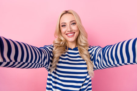 Portrait of optimistic funny girl with curly hairstyle wear striped pullover making selfie shouting blog isolated on pink color backgroundの写真素材