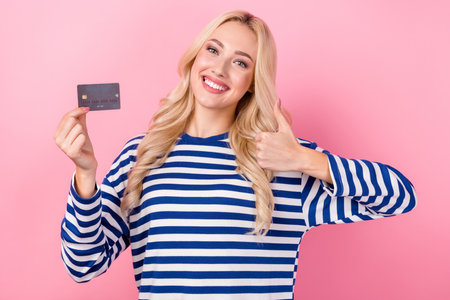 Photo of young girl curly hair wear striped pullover thumb up shopping using debit card money spending isolated on pink color backgroundの写真素材